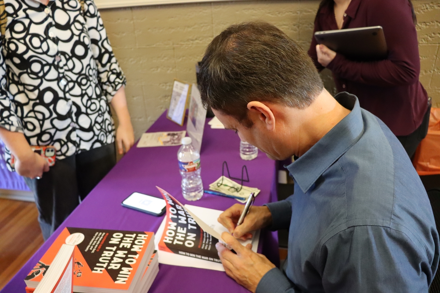 Samuel C. Spitale sitting at a table signing his book How to Win the War on Truth for an attendee.