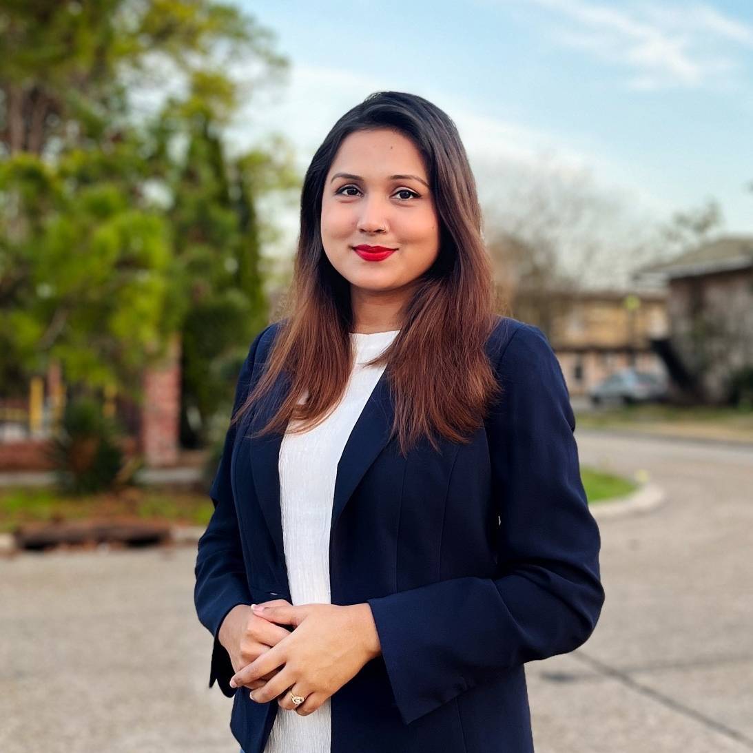 Moumita wearing a blue blazer with her hands crossed in front of her.